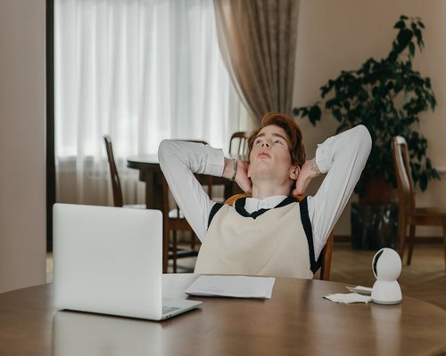 A person sitting comfortably at a tidy desk, taking a short break from looking at the laptop screen
